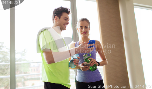 Image of happy woman and trainer showing smartphone in gym