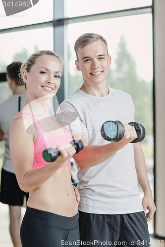 Image of smiling young woman with personal trainer in gym