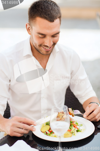 Image of happy man eating salad for dinner at restaurant
