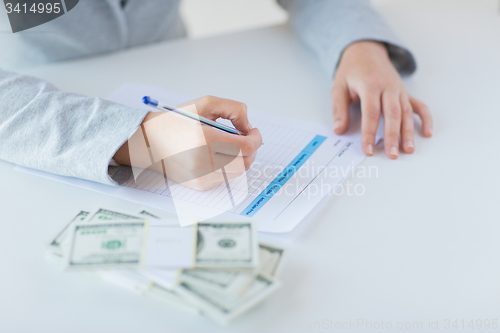 Image of close up of hands with money filling tax form