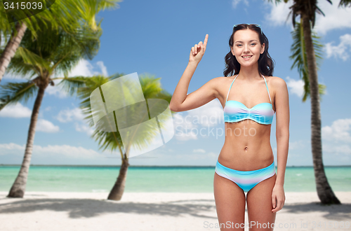 Image of happy woman in bikini pointing finger up on beach