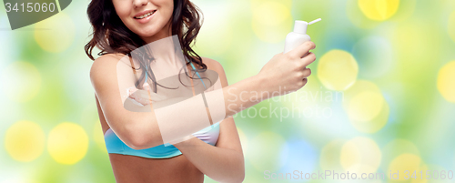 Image of happy young woman in swimsuit applying sunscreen