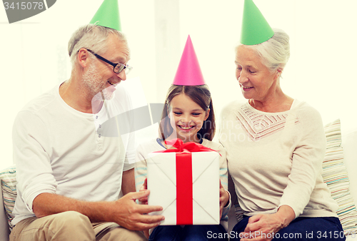 Image of smiling family in party hats with gift box at home