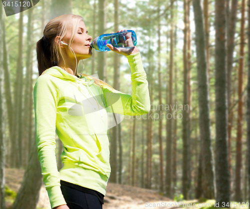 Image of woman drinking water after doing sports outdoors
