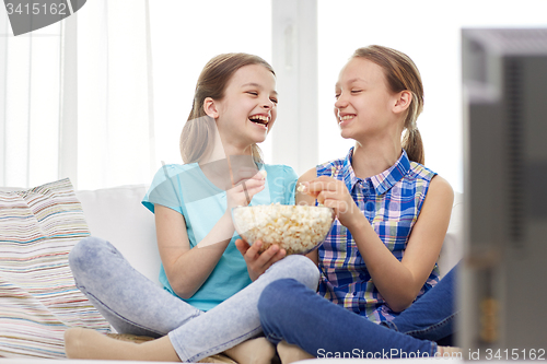Image of happy girls with popcorn watching tv at home