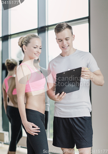 Image of smiling young woman with personal trainer in gym