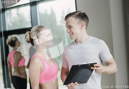 Image of smiling young woman with personal trainer in gym