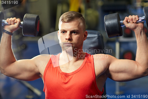 Image of young man with dumbbells flexing muscles in gym