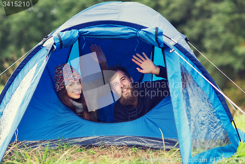 Image of smiling couple of tourists looking out from tent