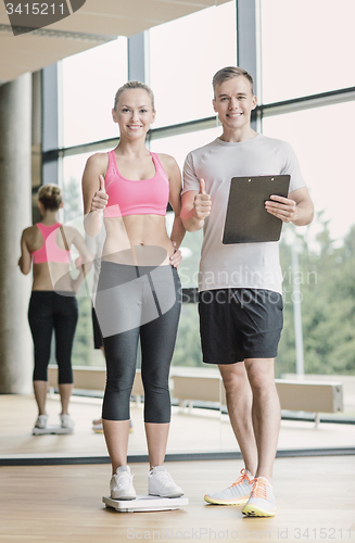 Image of smiling man and woman with scales in gym