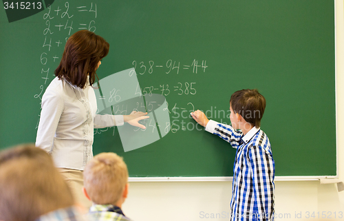 Image of schoolboy with math teacher writing on chalk board