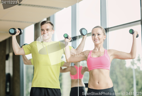 Image of smiling man and woman with dumbbells in gym