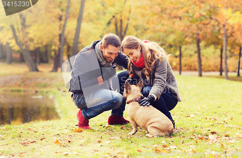 Image of smiling couple with dog in autumn park