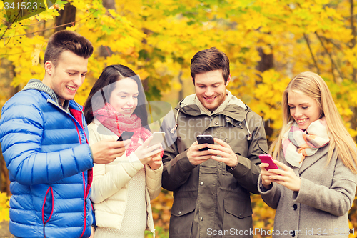 Image of smiling friends with smartphones in city park