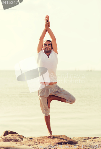 Image of smiling man making yoga exercises outdoors