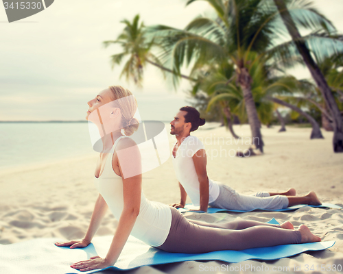 Image of happy couple making yoga exercises on beach
