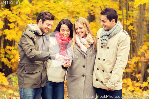Image of smiling friends with smartphones in city park