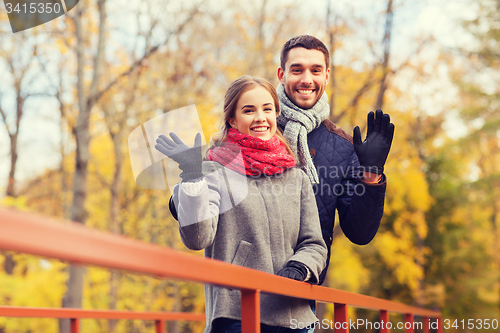 Image of smiling couple hugging on bridge in autumn park