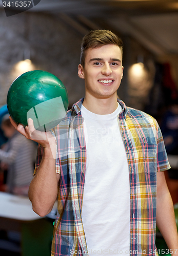 Image of happy young man holding ball in bowling club