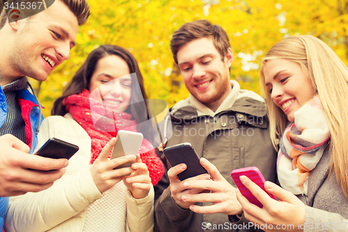 Image of smiling friends with smartphones in autumn park