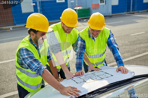 Image of close up of builders with blueprint on car hood