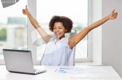 Image of happy african woman with laptop at office