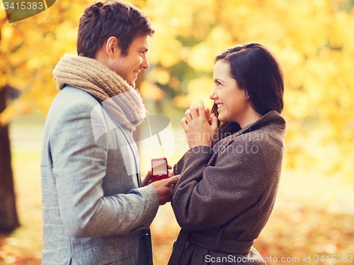 Image of smiling couple with red gift box in autumn park