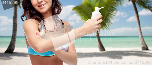 Image of happy young woman in swimsuit applying sunscreen