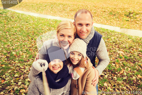 Image of happy family with selfie stick in autumn park