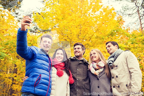 Image of smiling friends with smartphone in city park