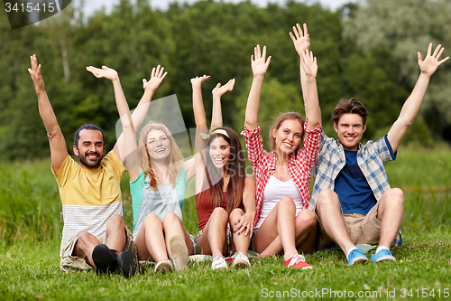 Image of group of smiling friends waving hands outdoors