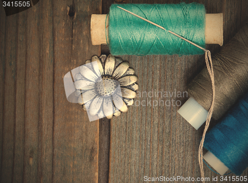 Image of vintage button flower, spool of thread and a sewing needle