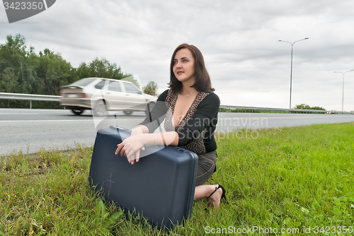 Image of Beautiful woman with suitcase waits on road