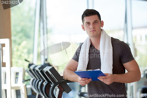 Image of trainer with clipboard standing in a bright gym