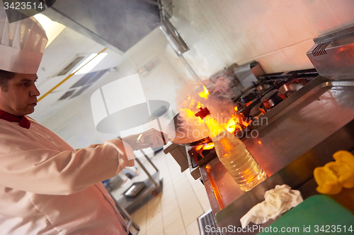 Image of chef in hotel kitchen prepare food with fire