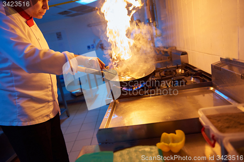 Image of chef in hotel kitchen prepare food with fire