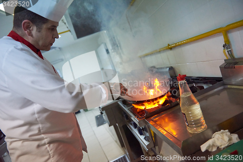 Image of chef in hotel kitchen prepare food with fire