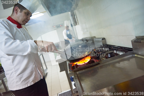 Image of chef in hotel kitchen prepare food with fire