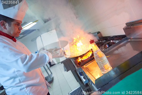 Image of chef in hotel kitchen prepare food with fire