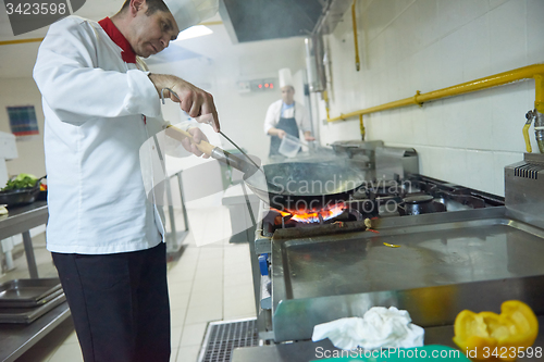 Image of chef in hotel kitchen prepare food with fire