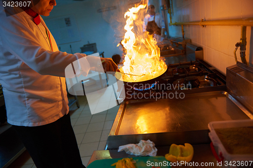 Image of chef in hotel kitchen prepare food with fire