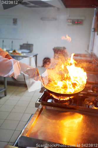 Image of chef in hotel kitchen prepare food with fire