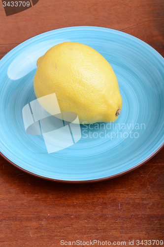 Image of Whole lemon on a blue plate on wooden background