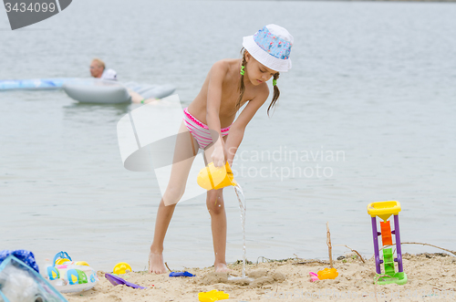 Image of Five-year girl on a beach pouring water from a bucket in the sand