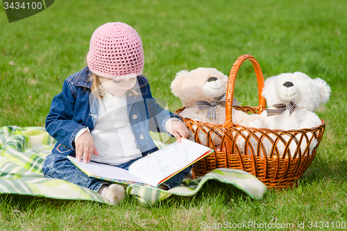 Image of Happy three year old girl reading a book on a picnic