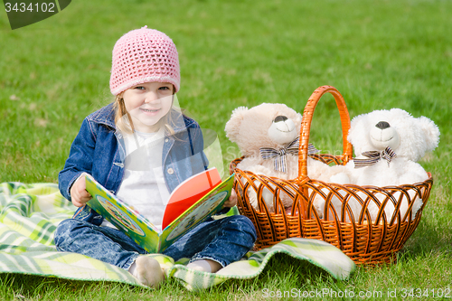 Image of Happy little girl with a book on a picnic