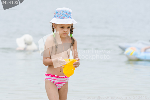 Image of Five-year girl on the beach carrying water in a bucket