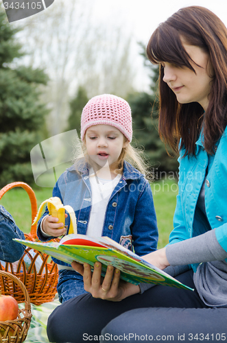 Image of Mom reading a book to a daughter at a picnic