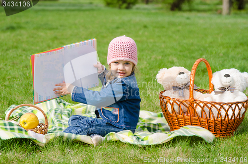 Image of The three-year girl showing a book on a picnic