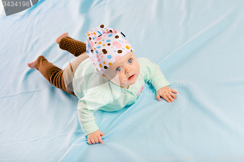 Image of blue-eyed baby in hat crawling